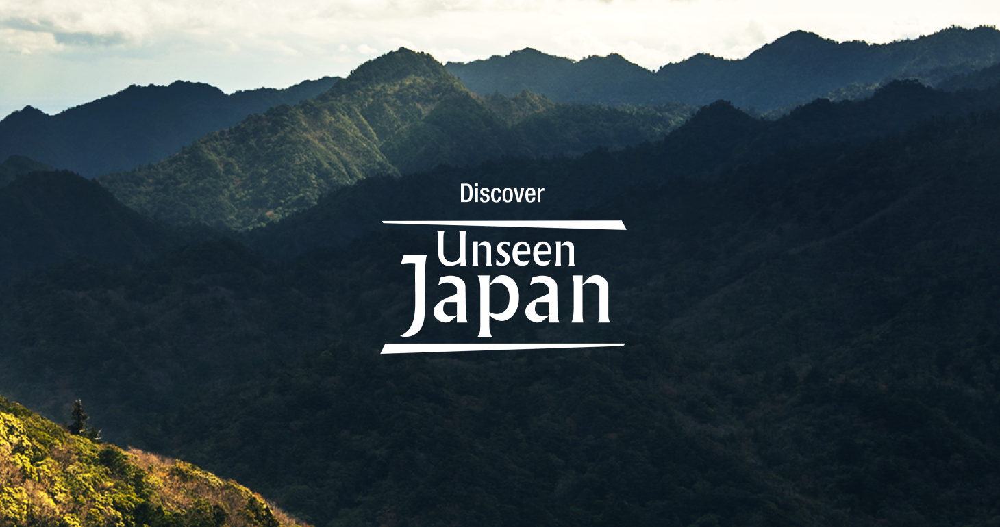 Hero image for the campaign showing a dramatic, sun-drenched mountain range meeting the sea, with the text "Discover Unseen Japan".