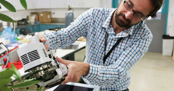 Man wearing glasses in a classroom holding scientific object