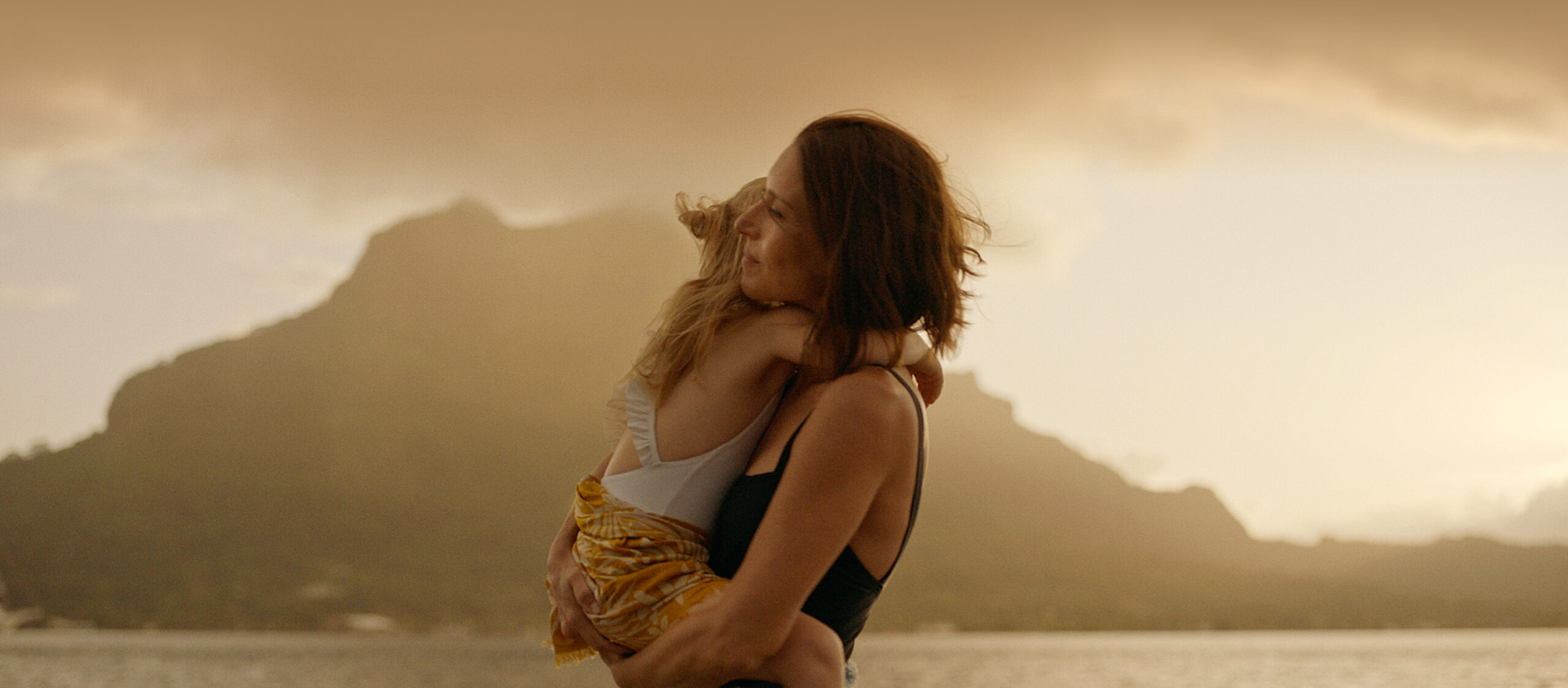 Brunette woman holding blonde child with big mountain silhouette behind