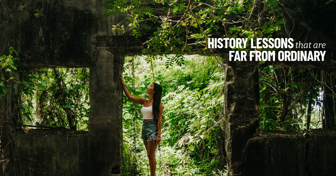 A woman explores the stone ruins of the Old Japanese Jail in Saipan, overgrown with lush green vines and trees.