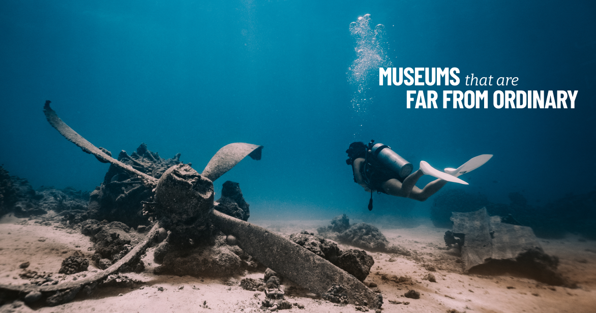 A scuba diver swims past the rusted propeller of a sunken aircraft on the sandy ocean floor in the Marianas.