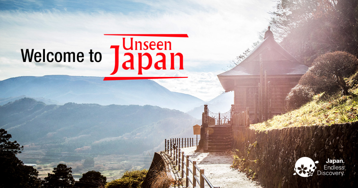 Promotional banner for the "Unseen Japan" campaign featuring a traditional wooden temple on a sunny hillside overlooking a vast mountain valley.